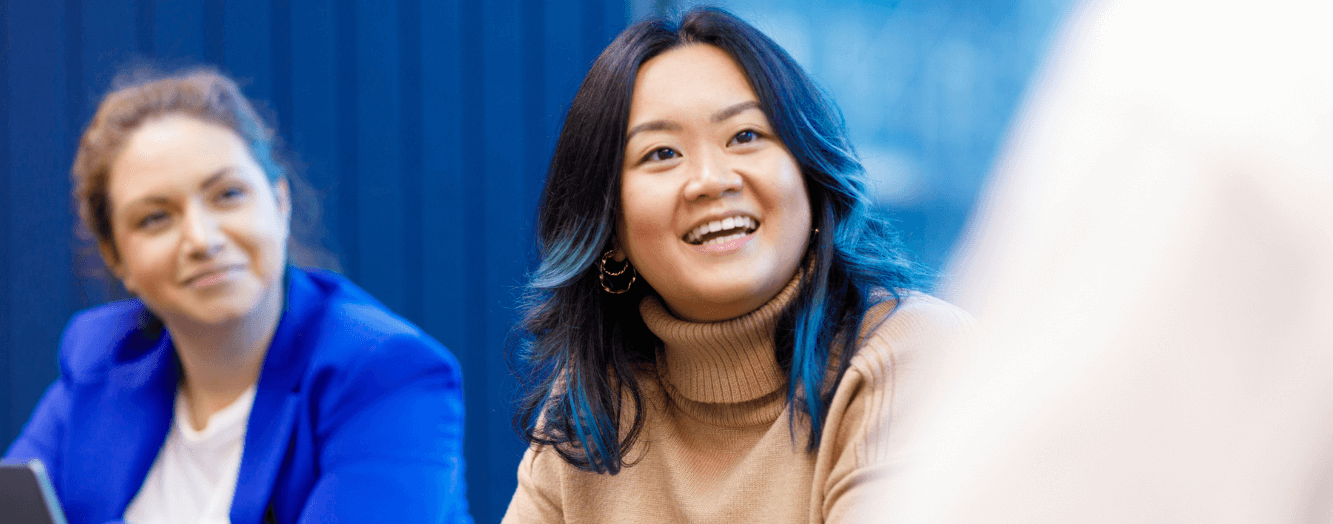 A colleague looking up while in a meeting She has long brown hair with blue tips.