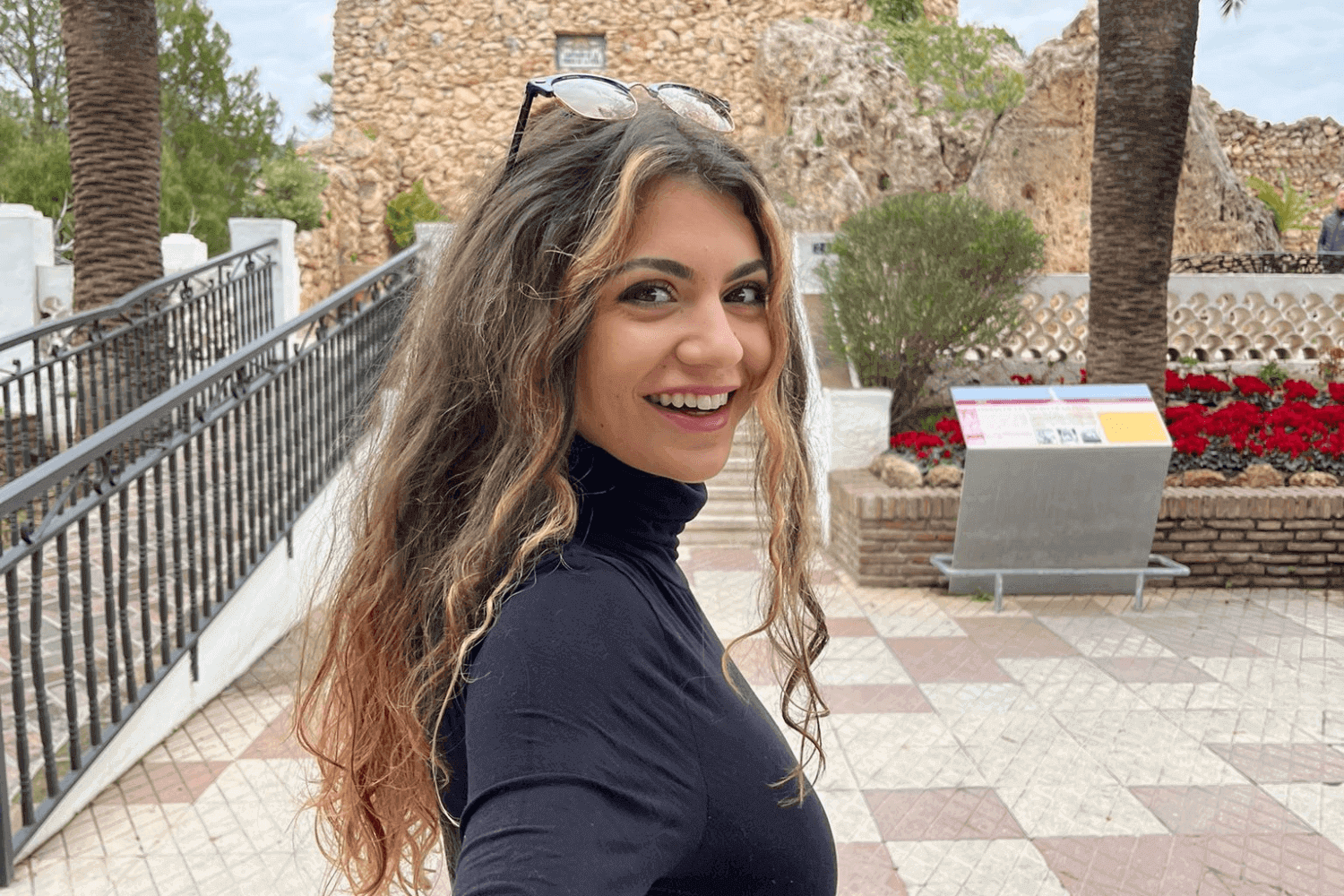 A young woman looking back at the camera. She has curly hair and sunglasses on her head. She is wearing a black polo neck. 