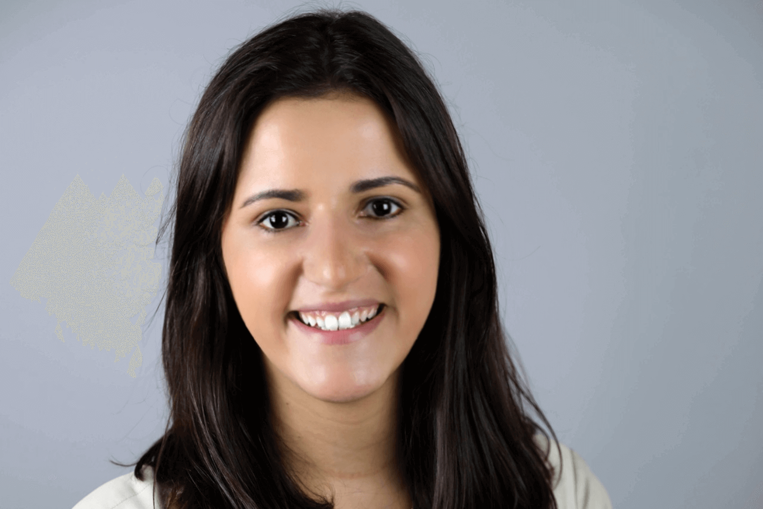 A woman smiling at the camera with her arms crossed. She is wearing a cream jacket and has shoulder length brown hair. 