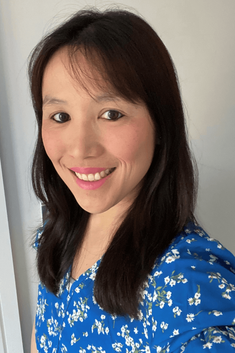A woman with shoulder length brown hair, wearing a blue and white flower pattern top. 