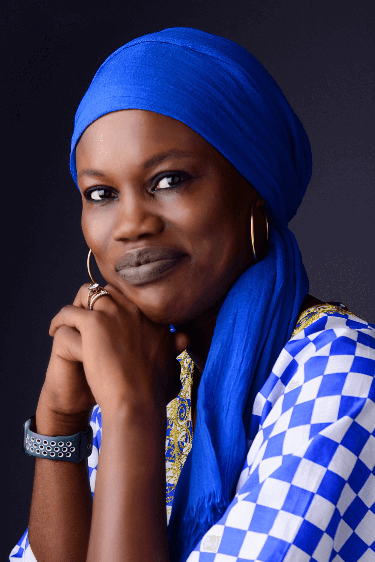 A woman resting her head on her hands She is wearing a blue and white checked top and a royal blue head covering. 