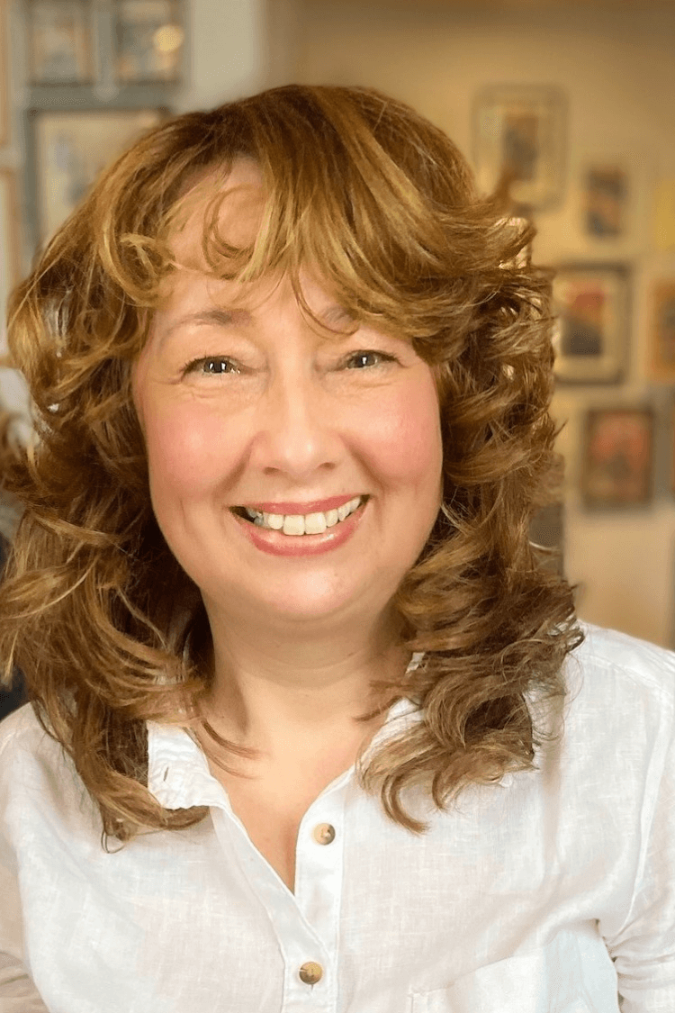 A woman with curly hair and wearing a white shirt, smiling at the camera. 