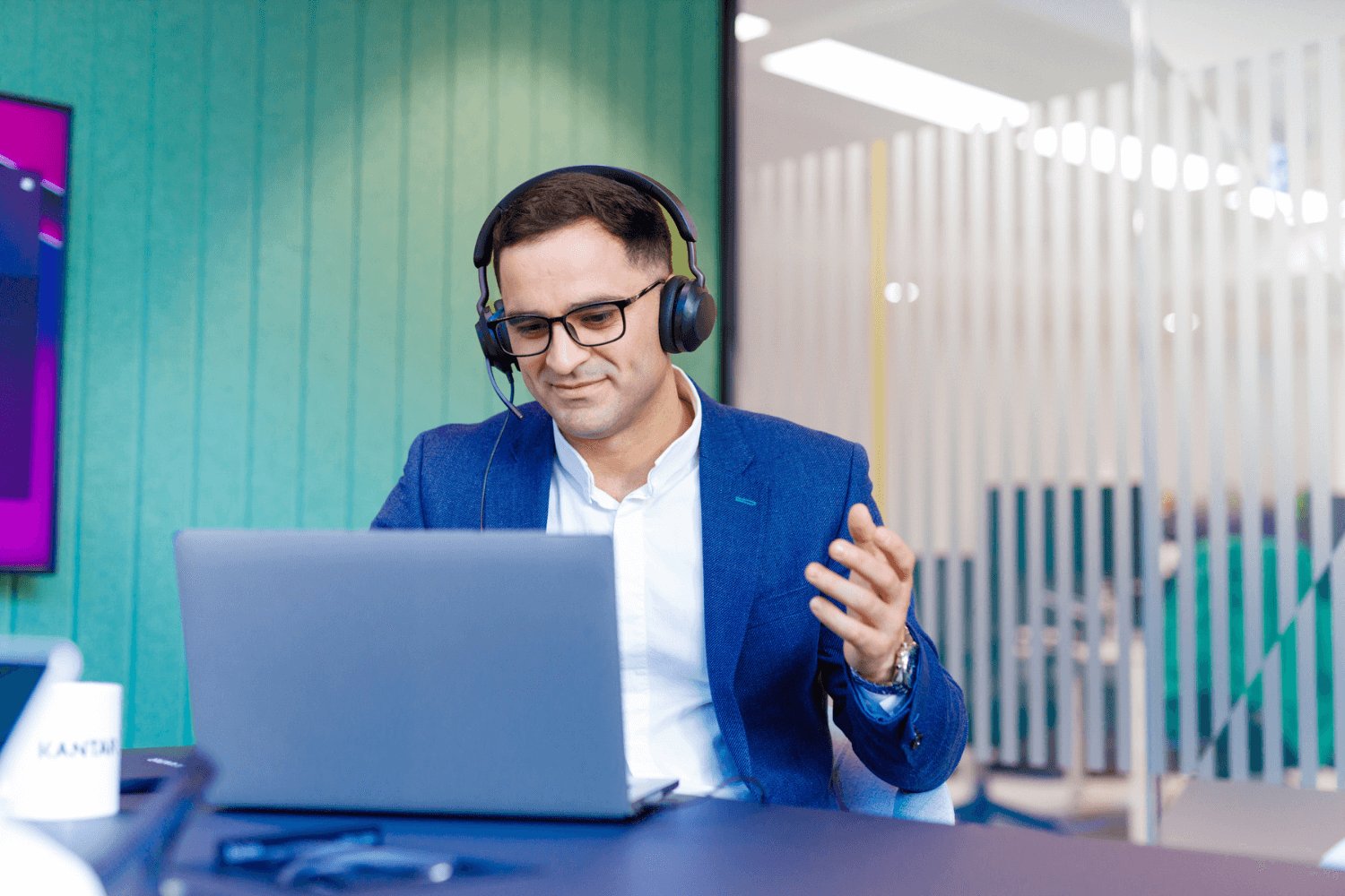 Ein Mann in marineblauer Jacke und weißem Hemd führt ein Telefongespräch. Er trägt ein Headset und gestikuliert mit der Hand. 