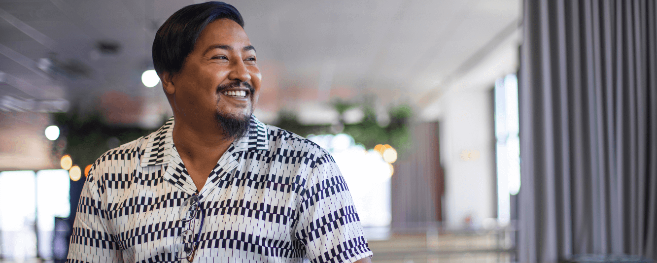 Ein Mann lächelt nach rechts. Er hat kurze braune Haare und trägt ein schwarz-weißes Hemd mit einem Muster, das Klaviertasten ähnelt.