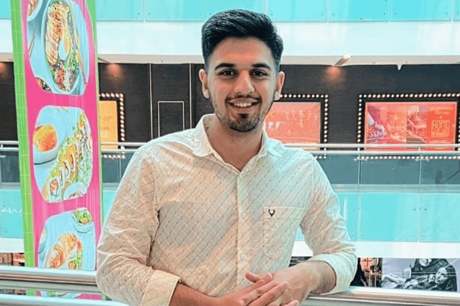 Ein Mann mit weißem Hemd und Jeans steht an einem Balkongeländer in einem Einkaufszentrum.