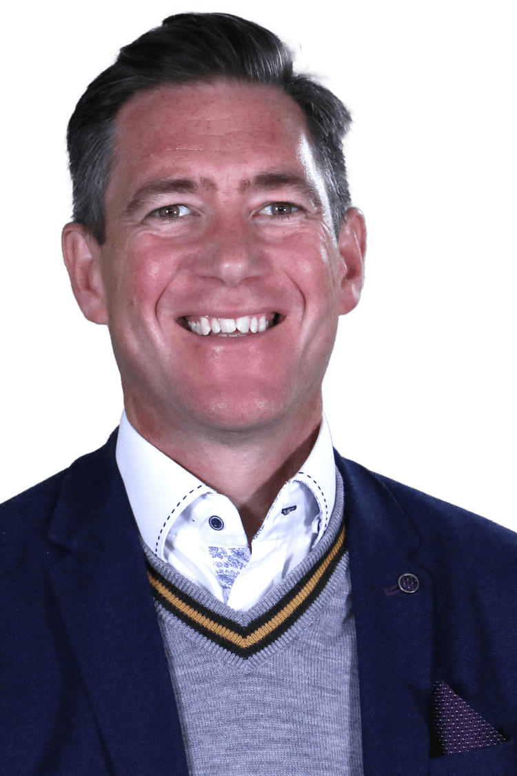 Ein Mann mit einem dunklen Blazer, einem grauen Pullover und einem weißen Hemd. 