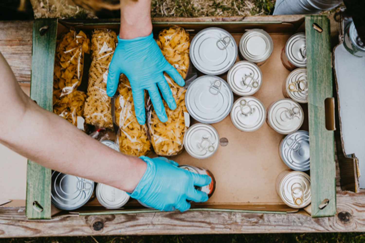 Un voluntario con guantes azules llena una caja de latas.