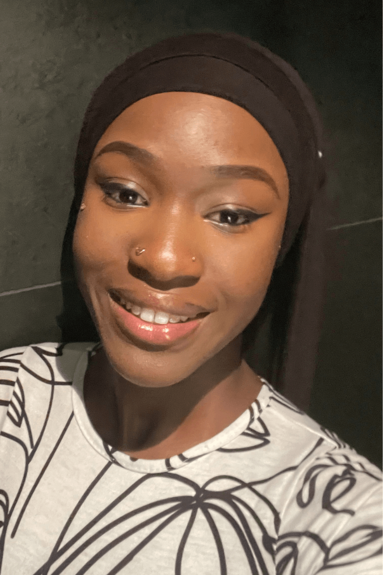 Una joven con una cinta negra en el pelo. Lleva una blusa blanca con un estampado lineal negro. 