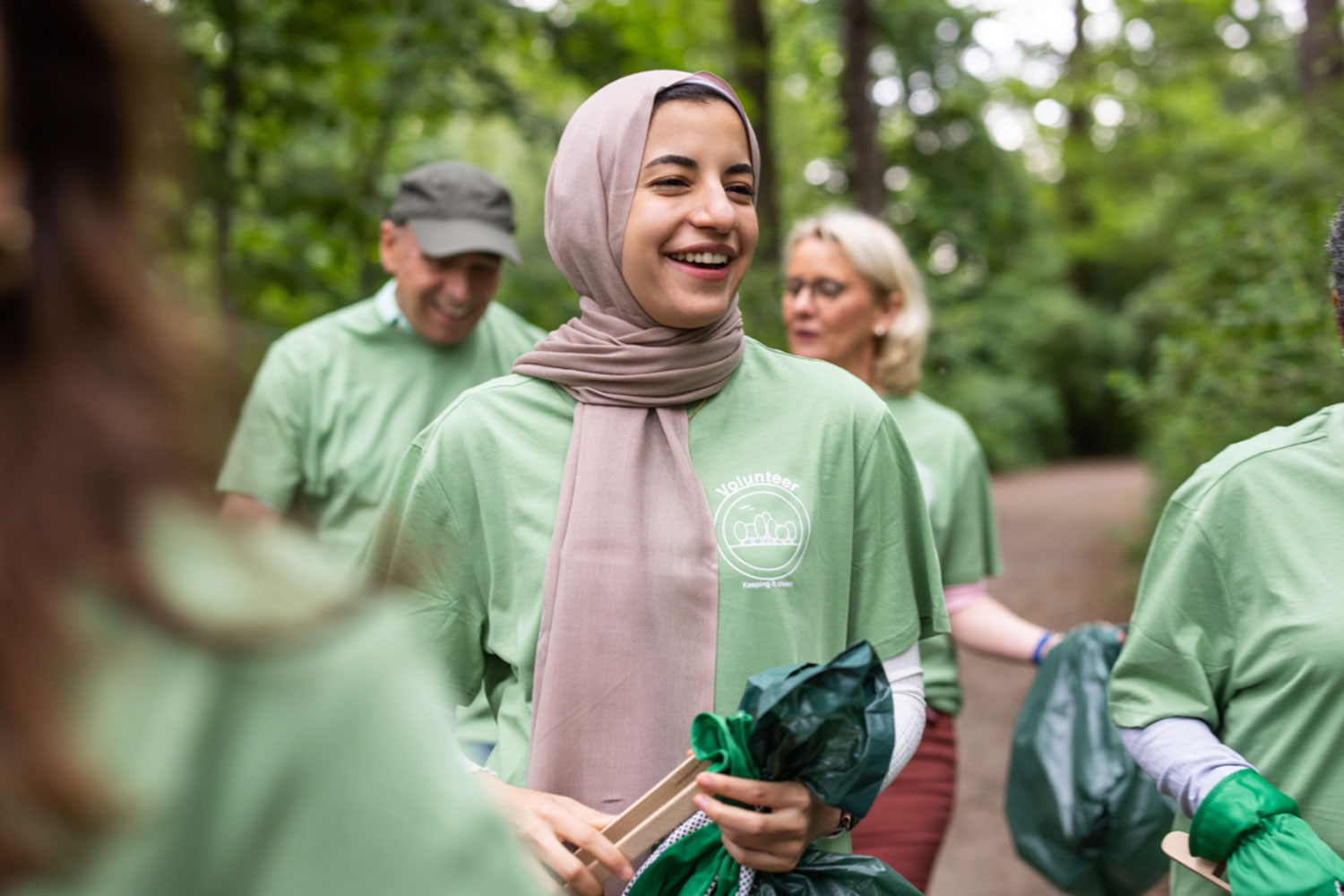 Een vrouw met een hoofddoek draagt een groen T-shirt en een vuilniszak