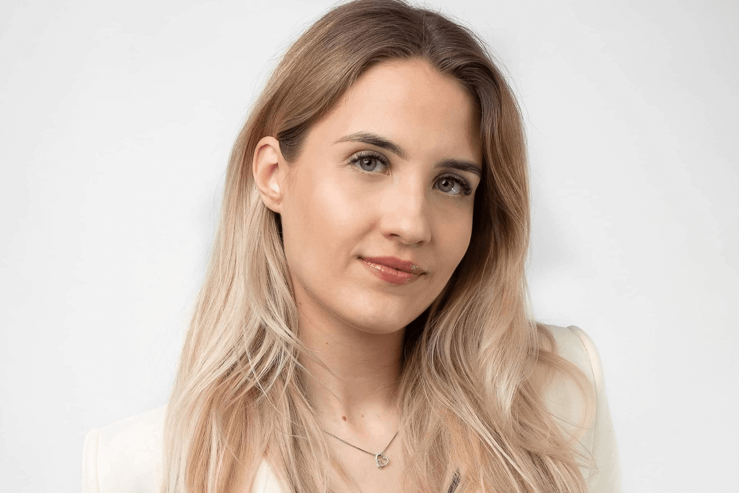 Een vrouw met lang blond haar, die een witte jas met knopen draagt, met daaronder een rood topje. 