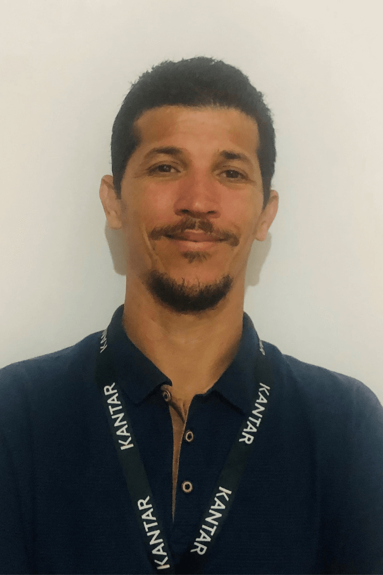 一名男子，深色头发，深棕色胡须。他身穿海军蓝衬衫，还可以看到他的 Kantar 挂绳。